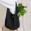 Dagne Dover Dash Grocery Tote in black over somebody's shoulder, containing groceries. 