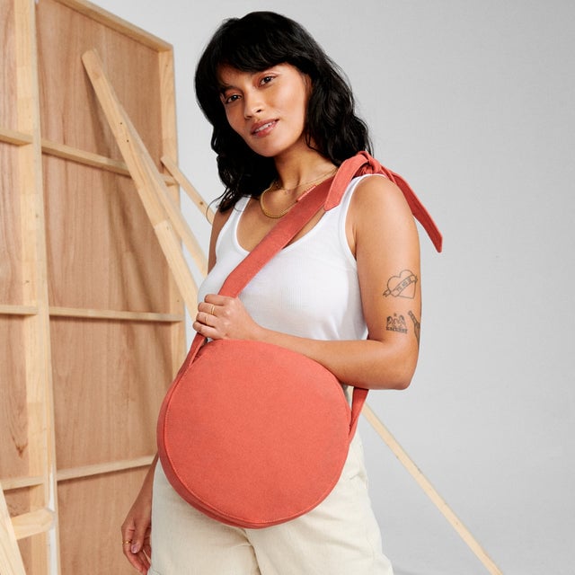 A woman holding the Luna Shoulder Bag in bright orange. 