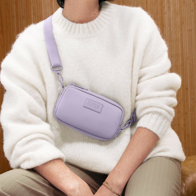 A woman wearing the Mara Phone Sling in light purple as a crossbody bag. 