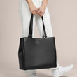 A model holding the 11.25 inch handle of the medium Allyn Tote in black. 