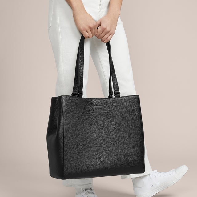 A model holding the 11.25 inch handle of the medium Allyn Tote in black. 