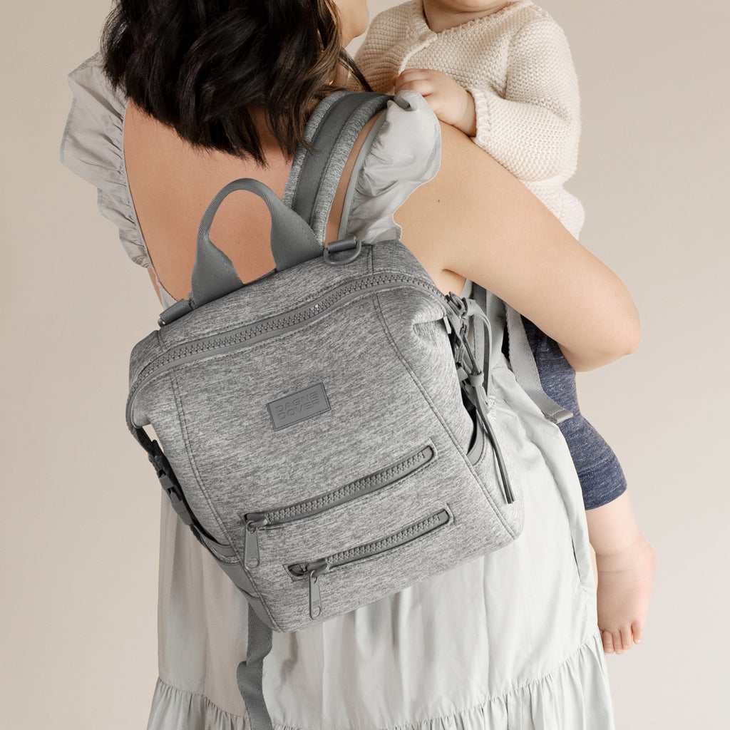 A woman wearing the small Indi Diaper Backpack in grey.
