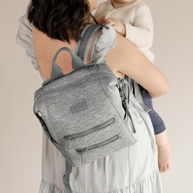 A woman wearing the small Indi Diaper Backpack in grey.